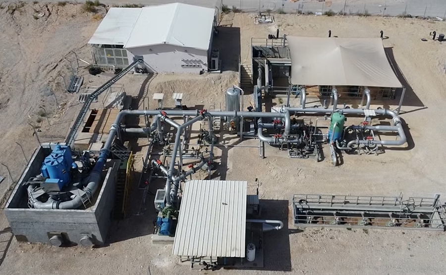 Aerial view of Augwind's 1 MW pilot plant showing a large compressor, lot of pipes and two buildings on a dusty patch of land.